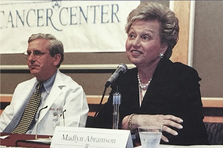 In a photo from late 1997, John Glick, MD, then director of the cancer center at Penn, sits at a table in front of microphones with philanthropist Madlyn Abramson.